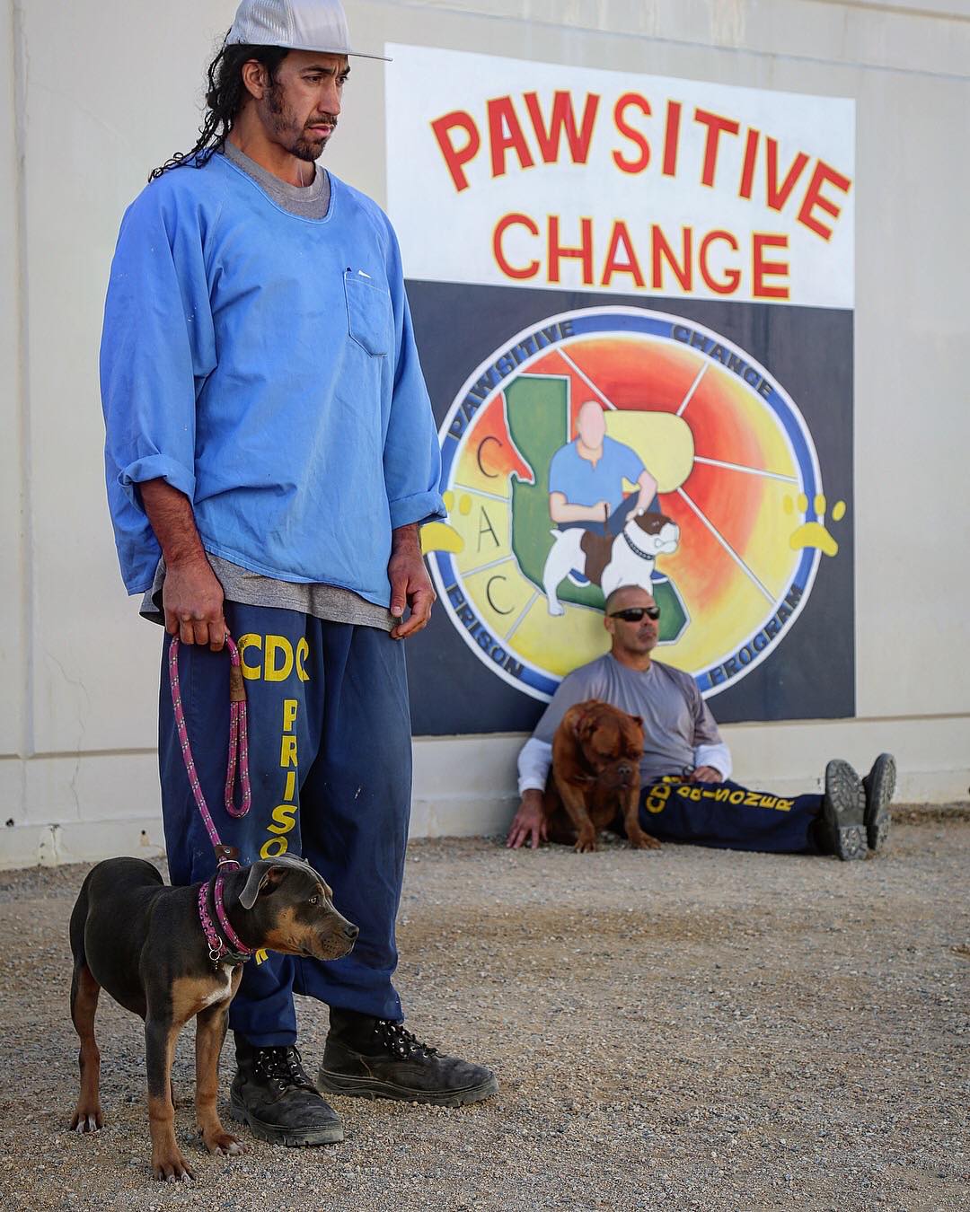 A Pawsitive Change student holding a leash with his dog in front of the program mural